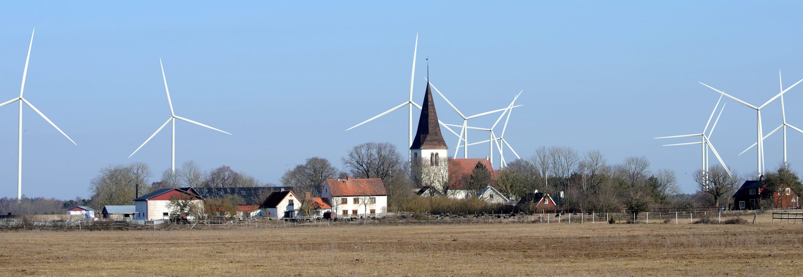 Bilden visar välbevarade Silte kyrka. Bakom kyrkan, mot klarblå himmel sticker 10 vindsnurror upp. 